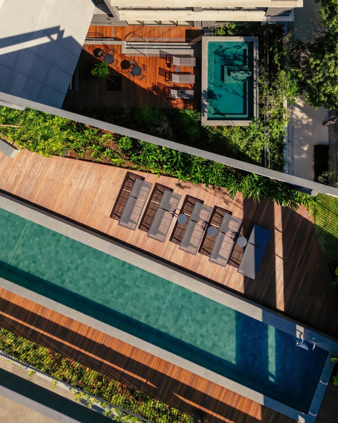 Área de Lazer Completa do ESQUINA Pinheiros – Piscinas e Deck em Madeira Vista aérea da área de lazer do ESQUINA Pinheiros com piscina, deck em madeira e espreguiçadeiras, empreendimento de alto padrão na Rua dos Pinheiros – SP